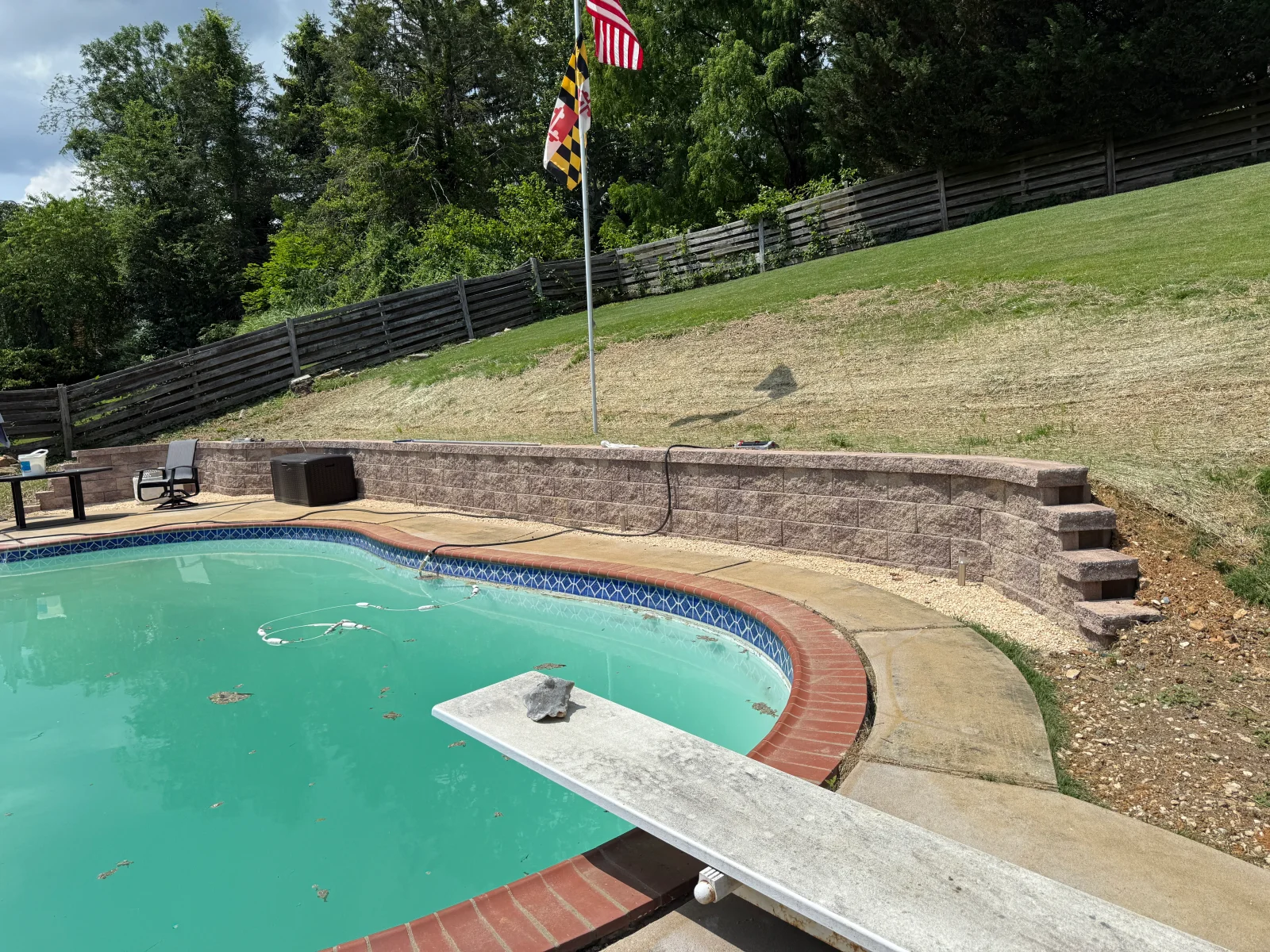 Gray segmental retaining wall with steps behind pool, concrete deck, and gravel base