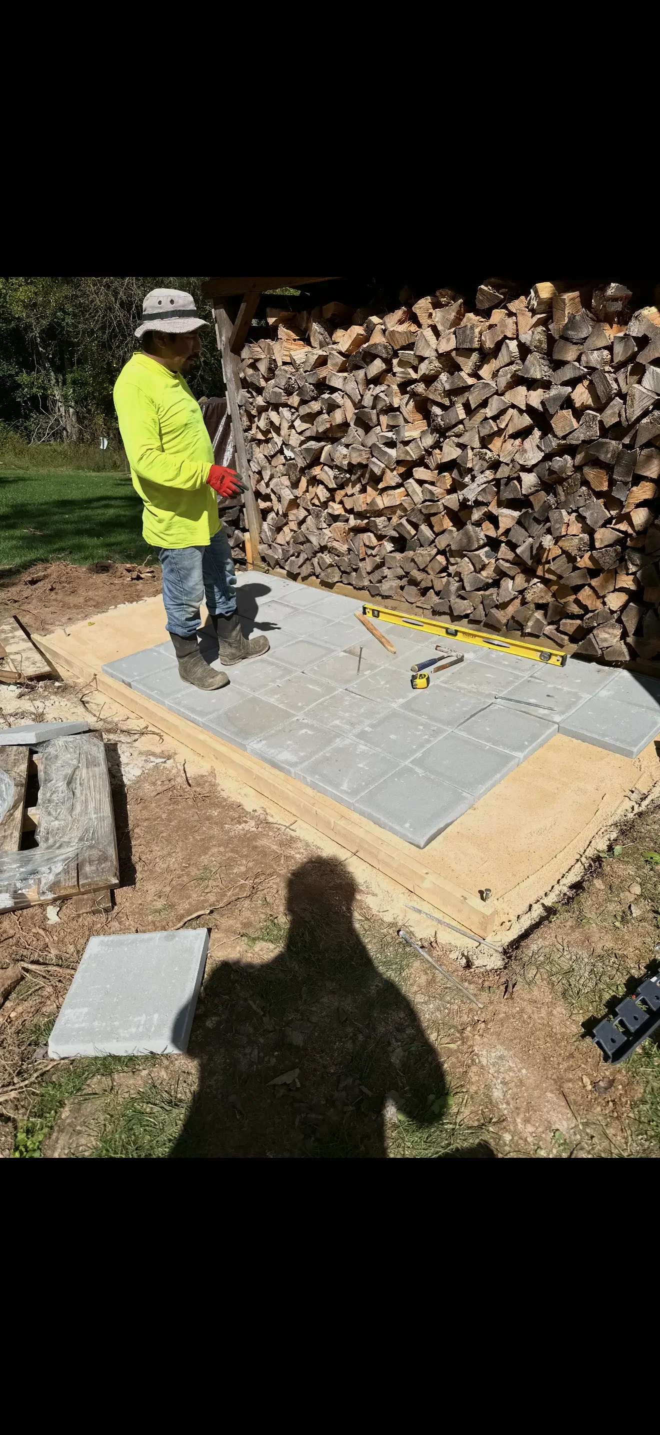 Worker installing gray concrete pavers on prepared base with level and measuring tools
