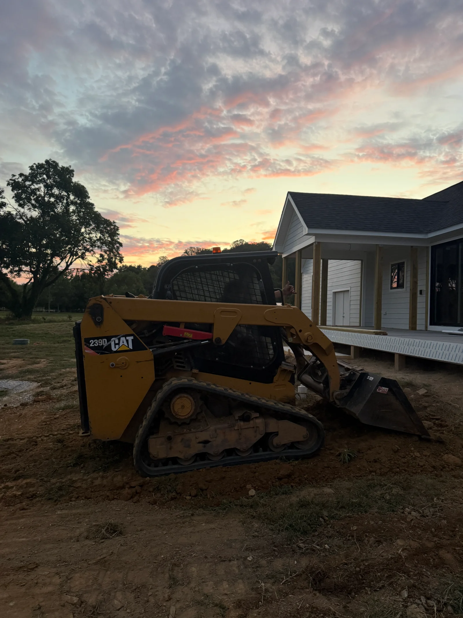 CAT 239D skid steer loader grading residential lot with modular home structure in background