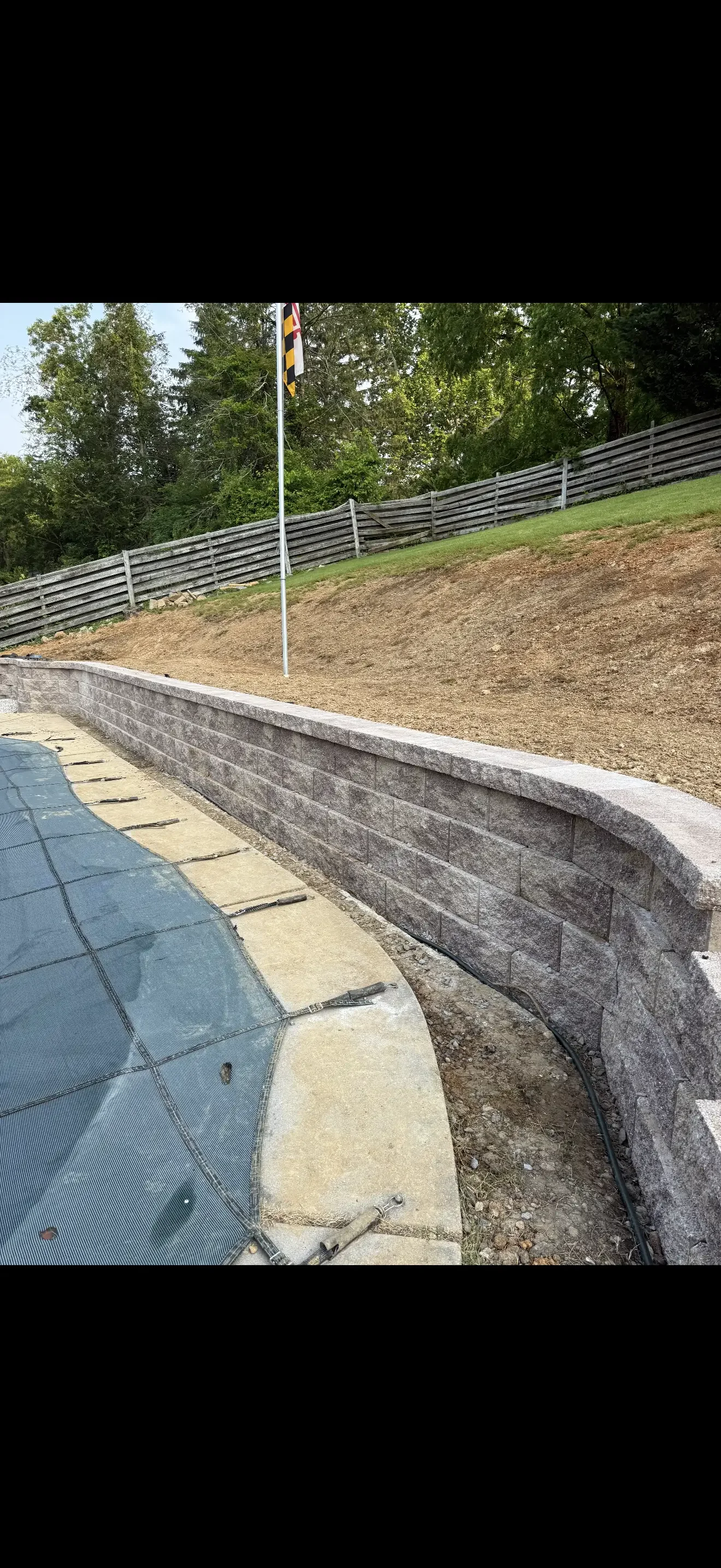 Concrete retaining wall with drainage pad and wooden rail fence on prepared arena site
