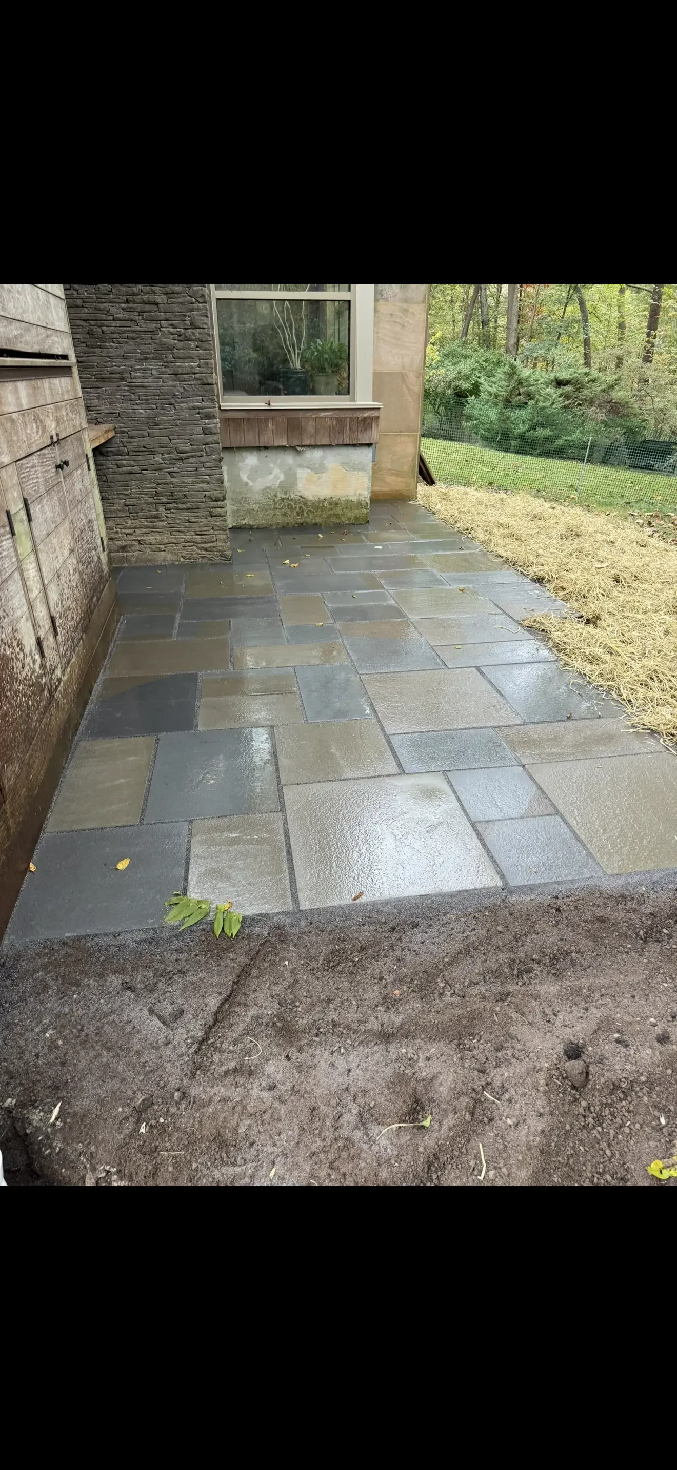 Multi-toned slate patio with running bond pattern installed next to stone house exterior