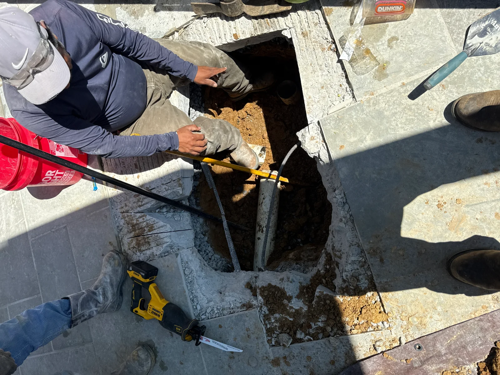 Worker excavating underground utility pit with hand tools and safety bracing visible