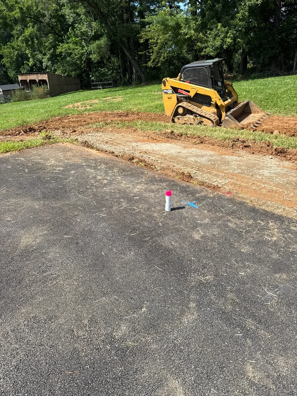 Compact track loader excavating and grading asphalt driveway with exposed soil base