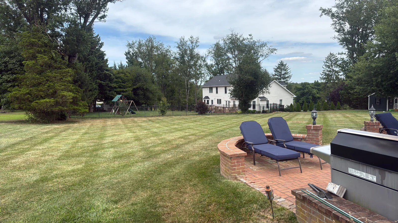 Curved brick patio with lounge chairs and integrated planter walls overlooking manicured lawn